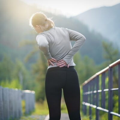 Back view of adult runner woman suffering from Backache or Sore waist after running.